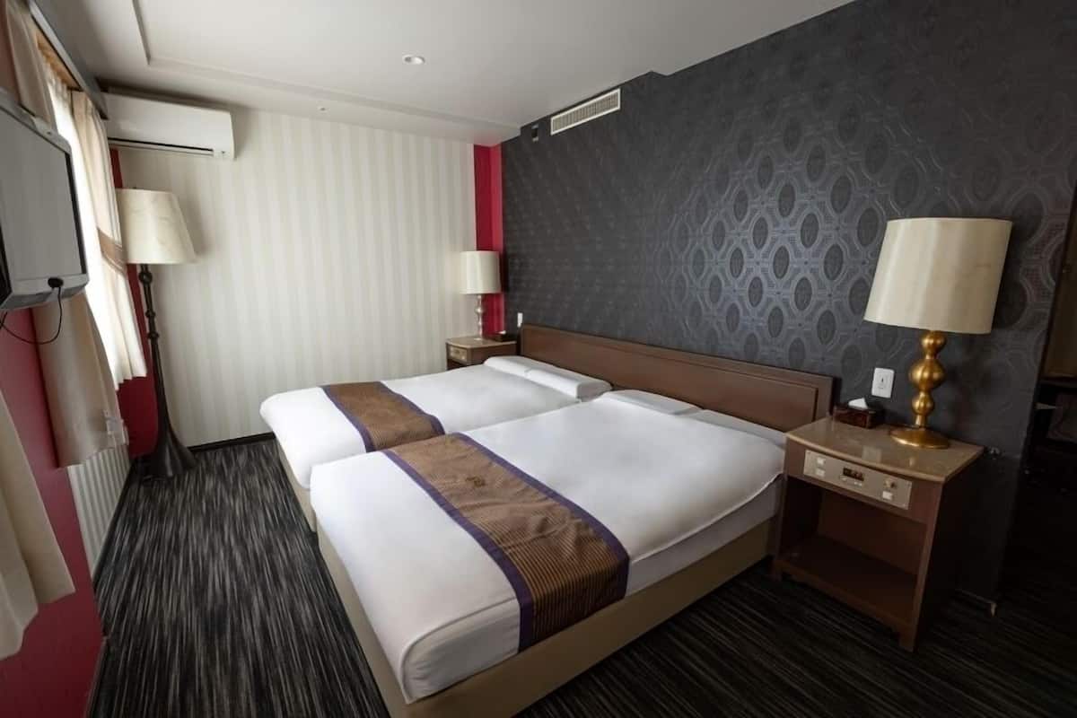 Une chambre d’hôtel avec un grand lit, deux tables de chevet, une lampe et une fenêtre avec des rideaux.