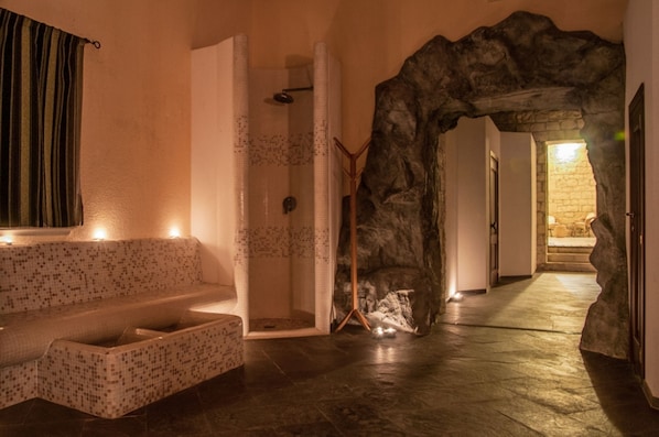 A spa area with a mosaic-tiled bench, a shower with a tiled wall, and a stone archway.