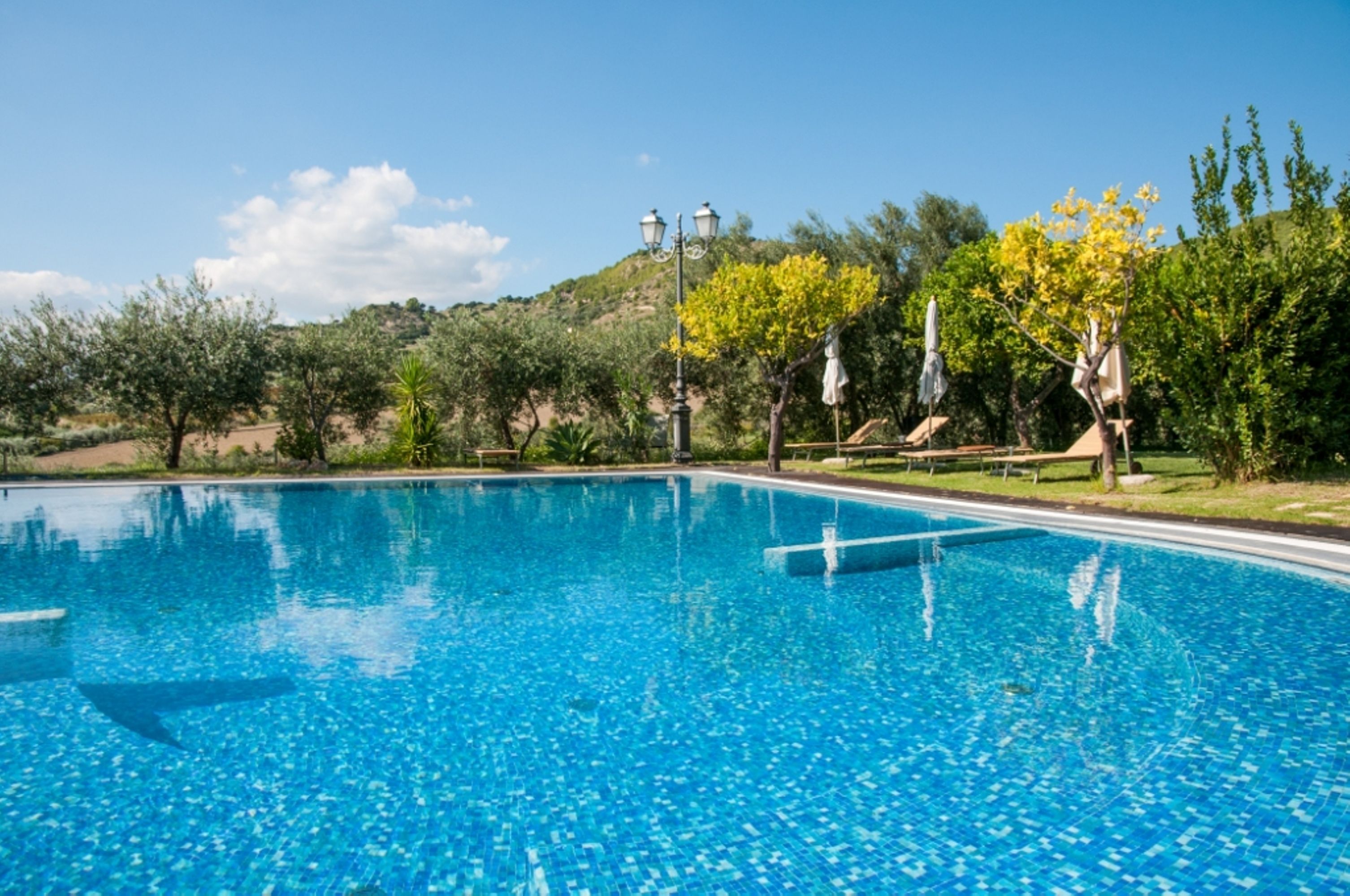 A clear blue swimming pool with a view of a hilly landscape and trees in the background.