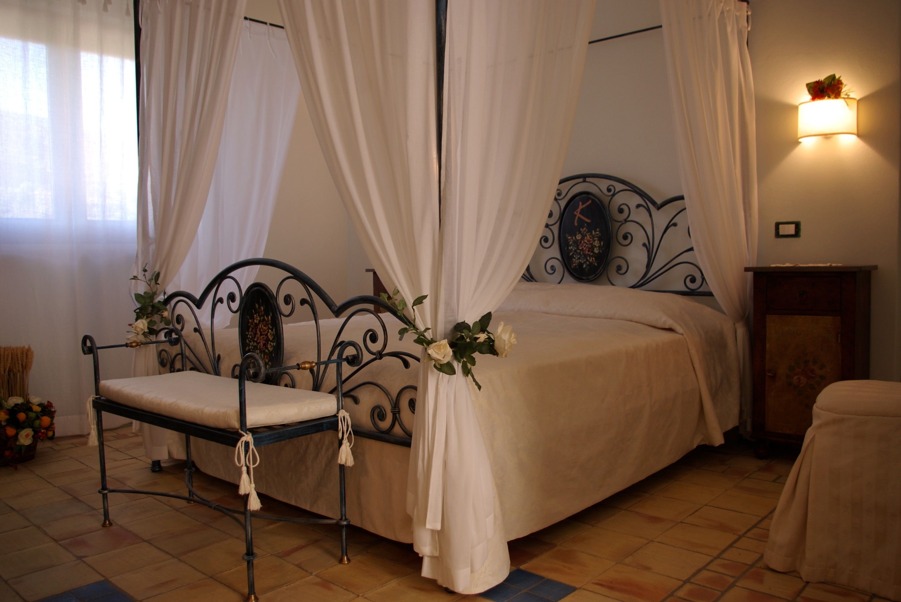 A four-poster canopy bed with a headboard, a bedside table, and a chair with a cushion.