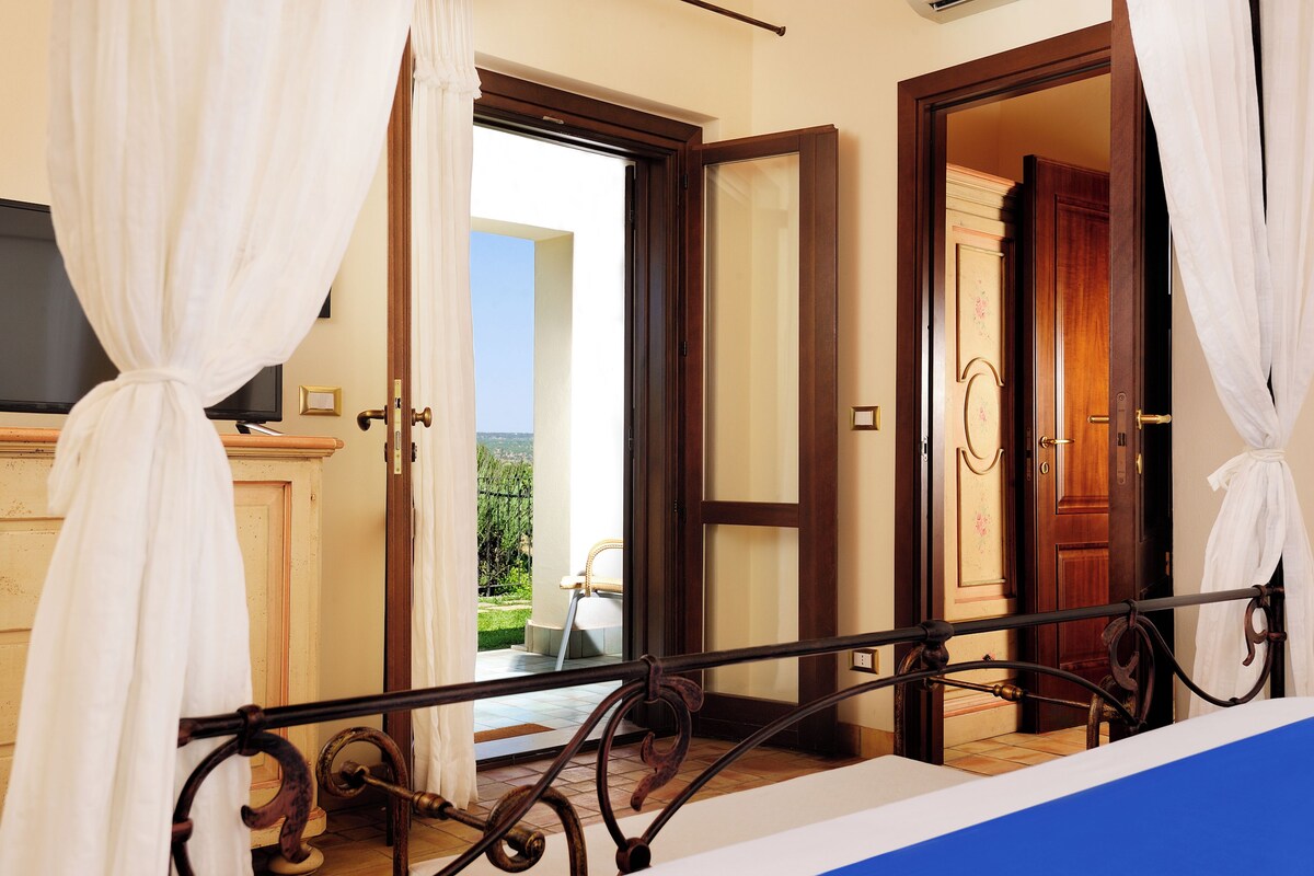 A hotel room with a balcony, a wooden door, and a view of the outdoors.