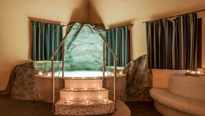 A spa area with a stone bath, a seating area, and curtains.