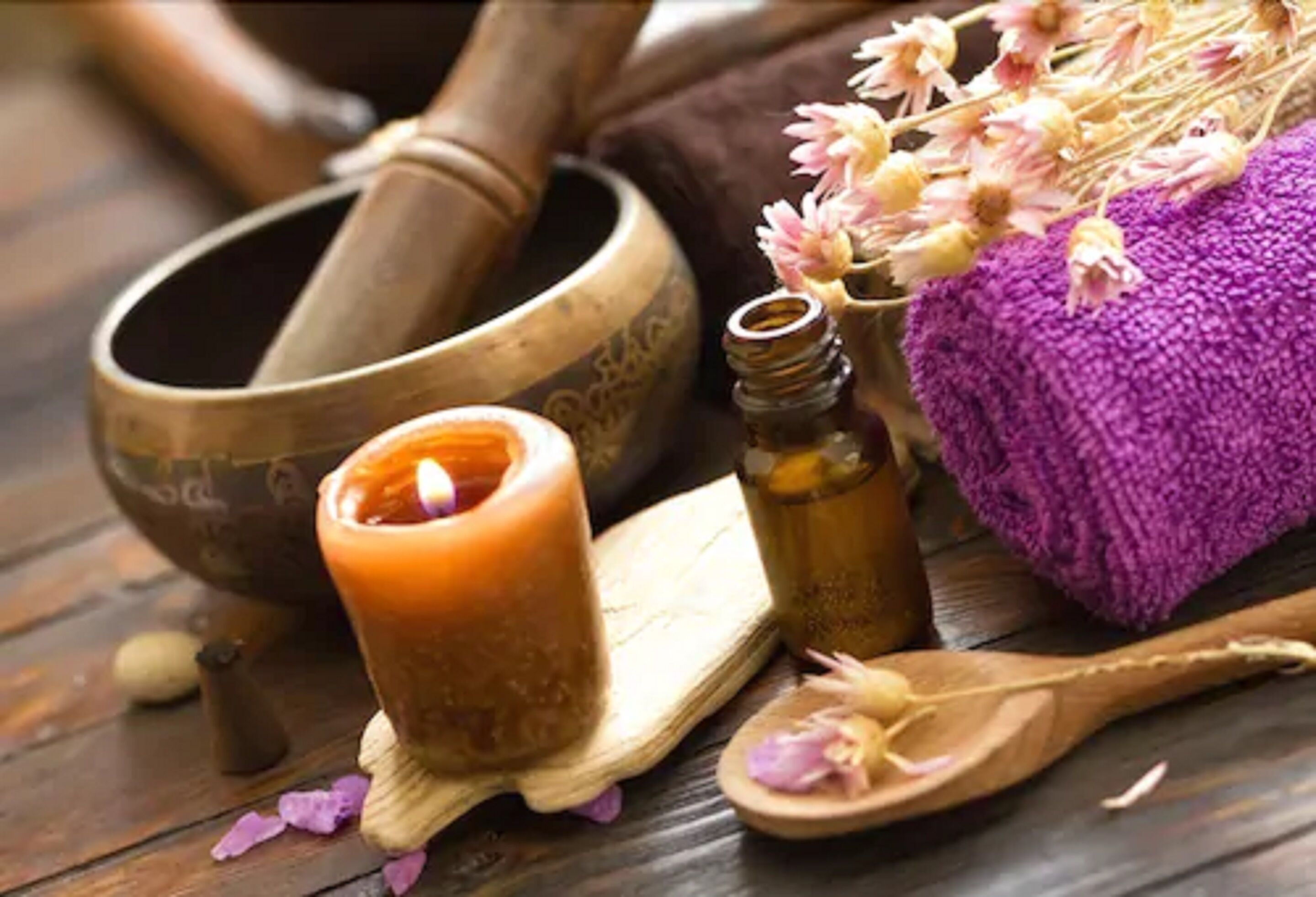 A wooden mortar and pestle, a candle, a small bottle, and a purple towel on a wooden surface.