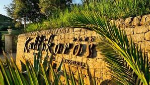 A stone wall with the text "KALIFORNIOS RESORT" and a palm tree in the foreground.