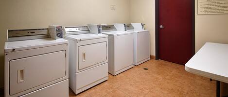 A laundry room with four white washers and dryers, a red door, and a sign indicating it's for guest use only.
