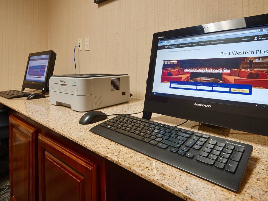 A hotel room with a desktop computer, a laptop, and a Brother printer on a granite countertop.