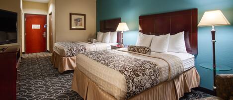 A hotel room with two beds, a TV, a desk, and a lamp.