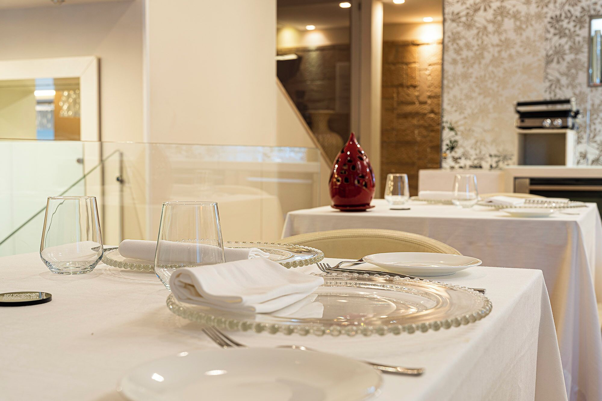 A dining table set with plates, glasses, cutlery, and a decorative vase.