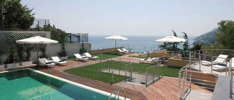 A rooftop pool area with lounge chairs and umbrellas, a clear view of the sea, and a wooden deck.