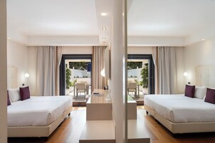 Habitación de hotel con dos camas, una mesita y vista al espacio exterior.