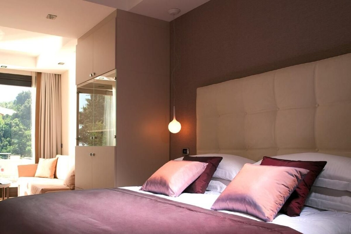 A modern bedroom with a large bed, a glass door leading to a balcony, and a wall-mounted light fixture.
