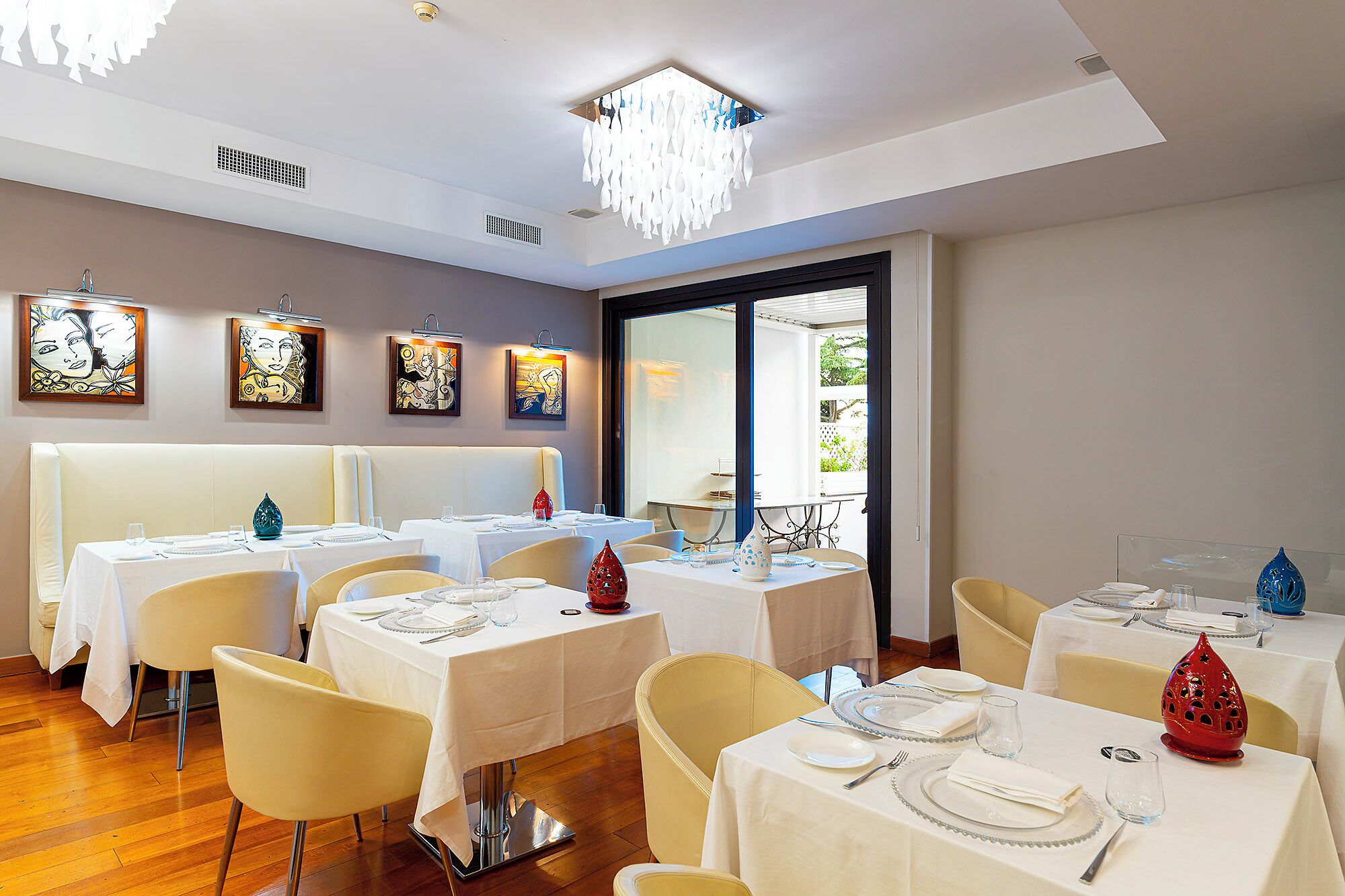 Un comedor con mesas dispuestas para el servicio, obras de arte en las paredes y vistas a través del ventanal.