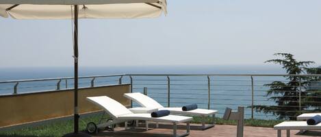Terraza con sillones de descanso y una sombrilla con vista a un cuerpo de agua.