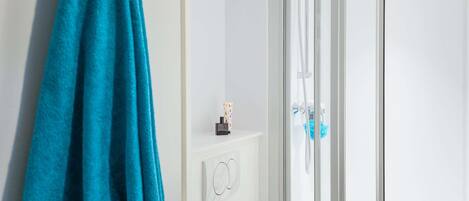 Un baño con cabina de ducha de vidrio, un perchero con una toalla azul y un pequeño estante con artículos de tocador.