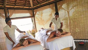 Een massageruimte met twee massagetafels, een houten plafond en een bamboescherm.
