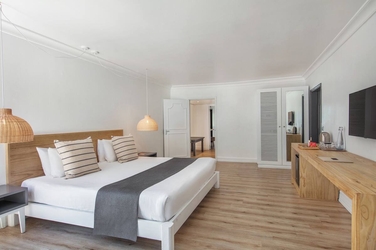 A modern bedroom with a large bed, bedside tables, a wooden desk, and a television.