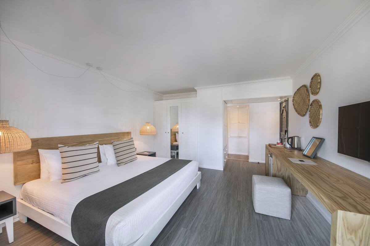 A modern hotel room with a large bed, bedside tables, a desk, and a flat-screen TV.