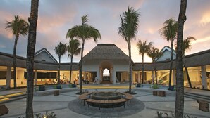 A resort courtyard with a central seating area, palm trees, and a thatched-roof building. - Ambre - Adults only (Belle Mare)