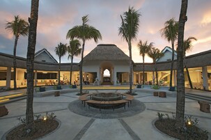 Un patio de resort con una zona de estar central, palmeras y un edificio con techo de paja.