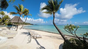 A beach resort with white lounge chairs, palm trees, a thatched-roof hut, and a clear blue sea. - Ambre - Adults only (Belle Mare)