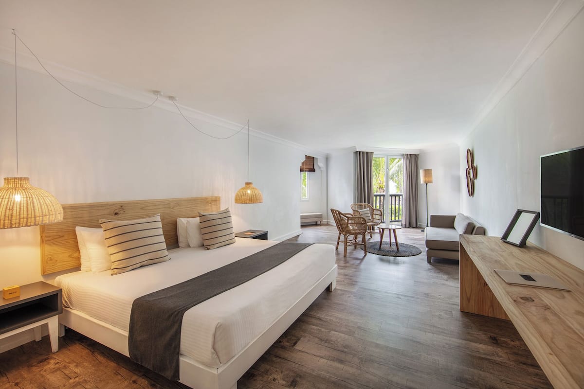 A modern hotel room with a large bed, wooden headboard, bedside lamps, a desk, and a TV.
