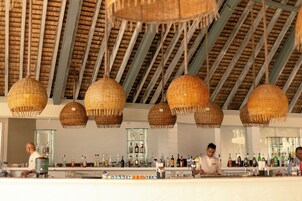 Una zona de bar con lámparas colgantes de mimbre, un bartender y una barra bien abastecida.