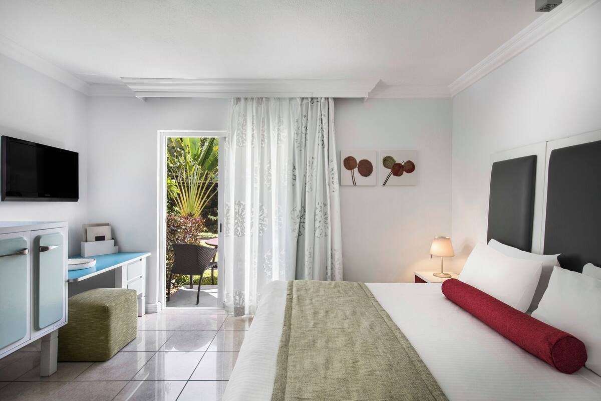 A hotel room with a bed, a desk, a TV, and a view of the outdoors.