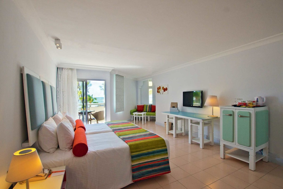 A hotel room with a bed, a desk, a TV, and a view of the ocean.