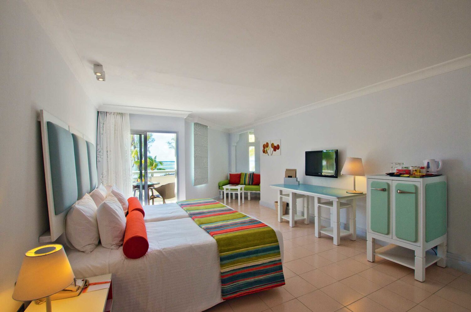 A hotel room with a bed, a desk, a TV, and a view of the ocean.