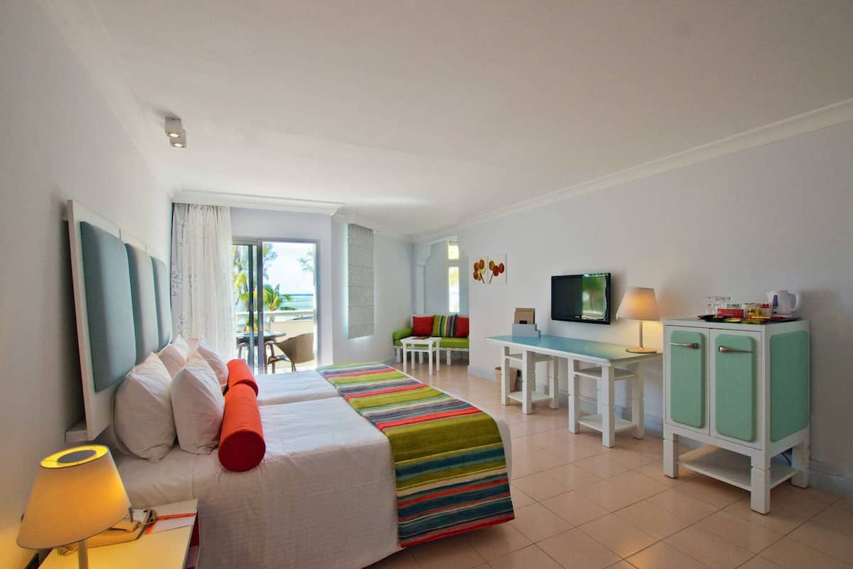 A hotel room with a bed, a desk, a TV, and a view of the ocean.
