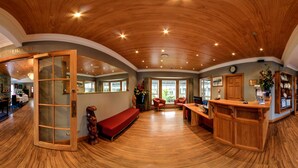 A spacious lobby with wooden floors and a high ceiling, a reception desk, a seating area, and a view of the outside. - Wai Ora Lakeside Spa Resort (Rotorua)
