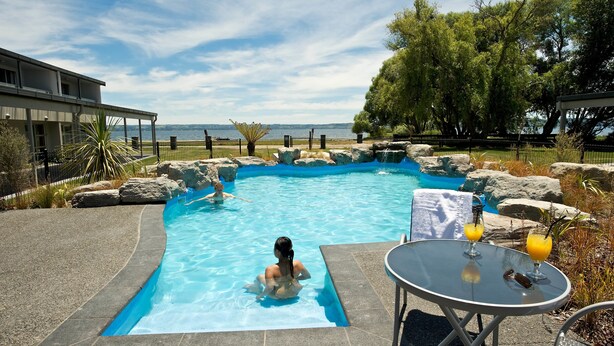 A swimming pool with a view of the sea, surrounded by rocks and trees. - Wai Ora Lakeside Spa Resort (Rotorua)