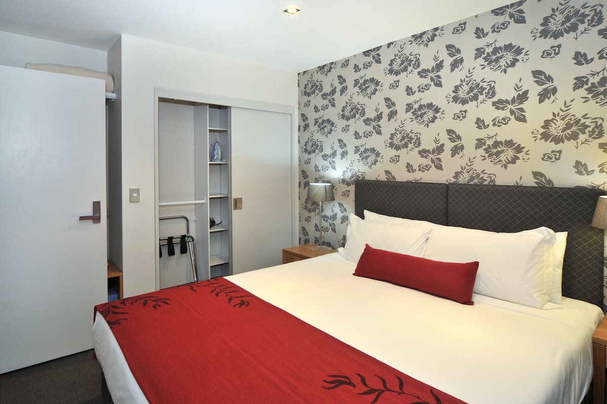A hotel room with a bed, a wardrobe, a nightstand, and a wall with floral wallpaper.