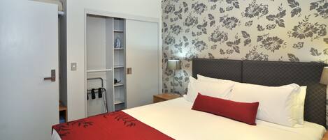 A hotel room with a bed, a wardrobe, a nightstand, and a wall with floral wallpaper.