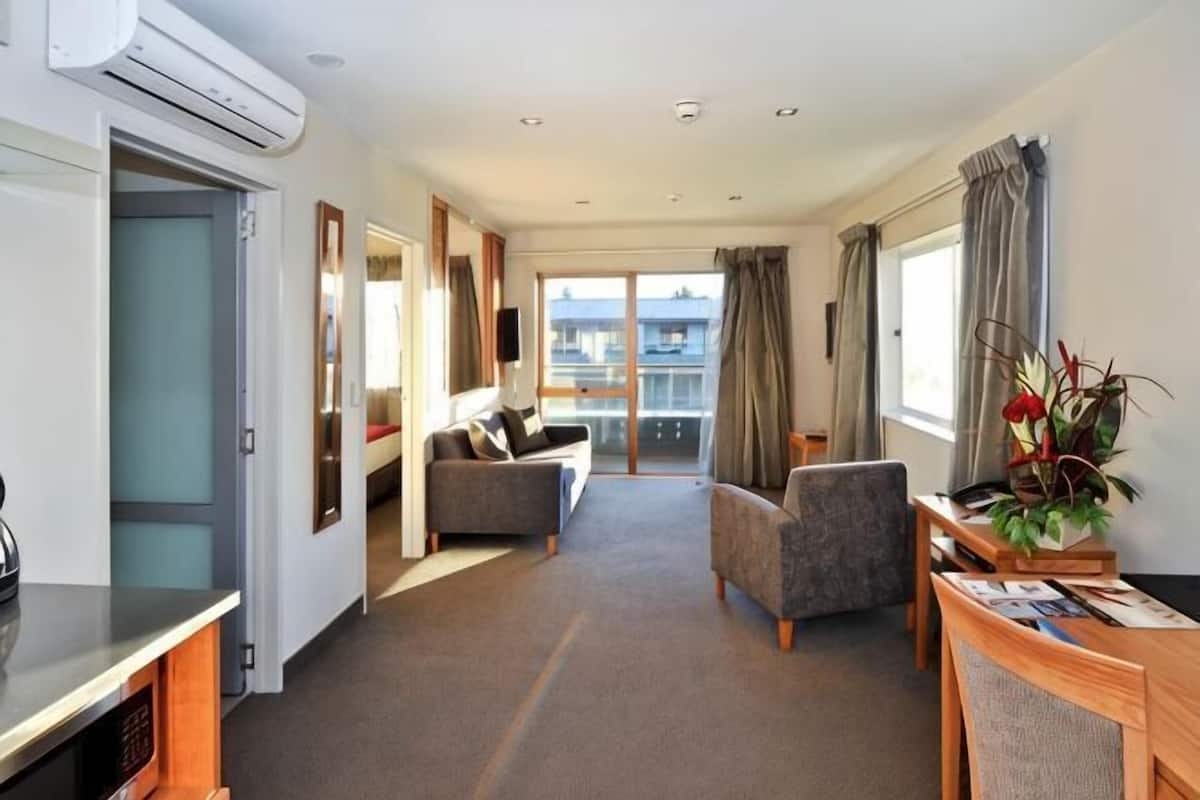 A hotel room with a sofa, armchair, dining table, and a balcony with curtains.