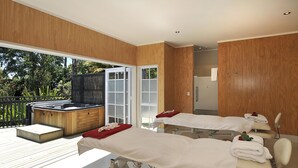 A spa room with two treatment beds, a hot tub, and a wooden deck with a view of greenery. - Wai Ora Lakeside Spa Resort (Rotorua)
