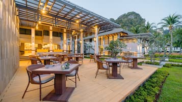 An outdoor dining area with wooden tables and chairs, a covered seating area, and a view of a mountain.