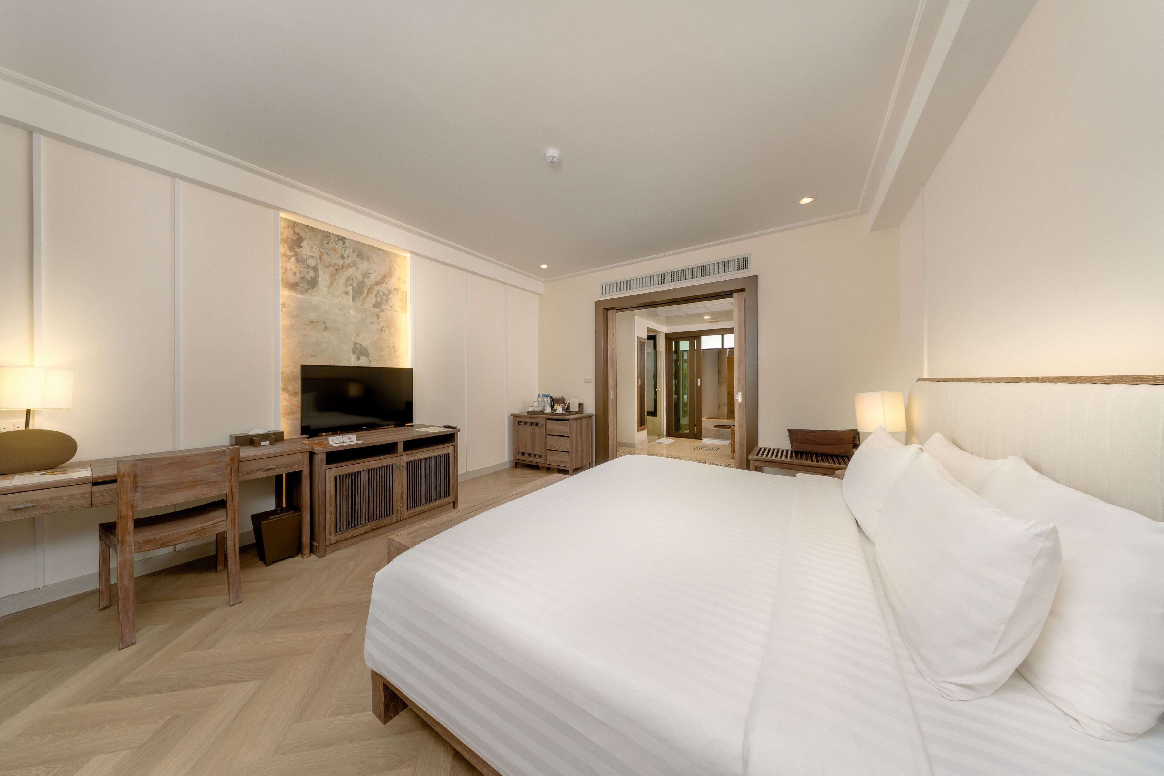 Quarto de hotel com uma cama grande, uma mesa com televisão, um espelho e uma porta que dá para outro cômodo.
