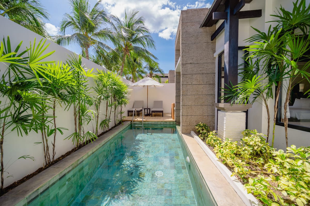 Piscina com água azul cristalina, rodeada por plantas verdes exuberantes e palmeiras.