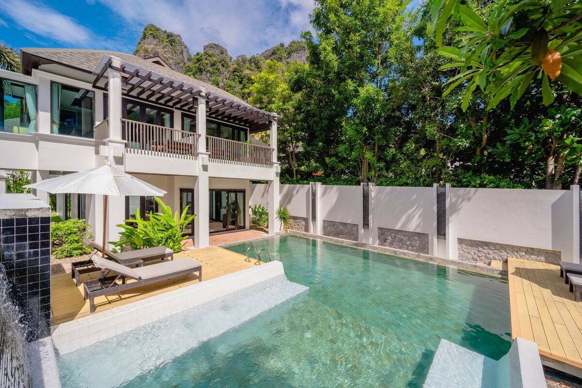Uma casa de dois andares com piscina, móveis de exterior e uma cascata.