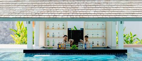 A poolside bar with a tiled roof, shelves of bottles, and a pool.