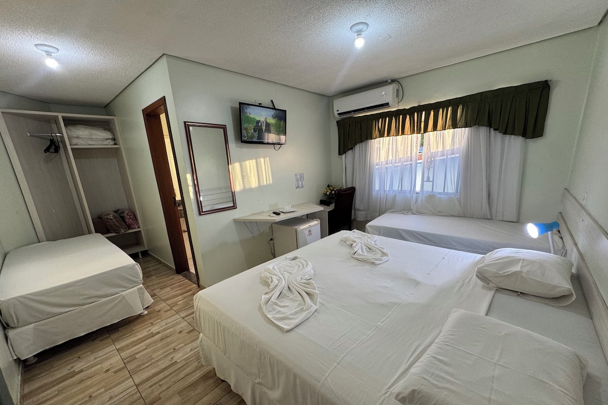 Une chambre d’hôtel avec deux lits, un bureau, un miroir, un appareil de climatisation et une fenêtre avec des rideaux.