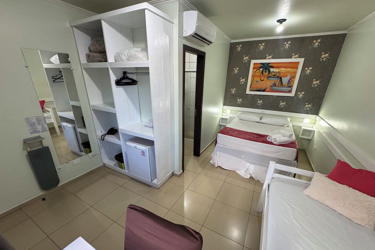 Une chambre d’hôtel avec un lit, un bureau, une armoire, un miroir et un tableau au mur.