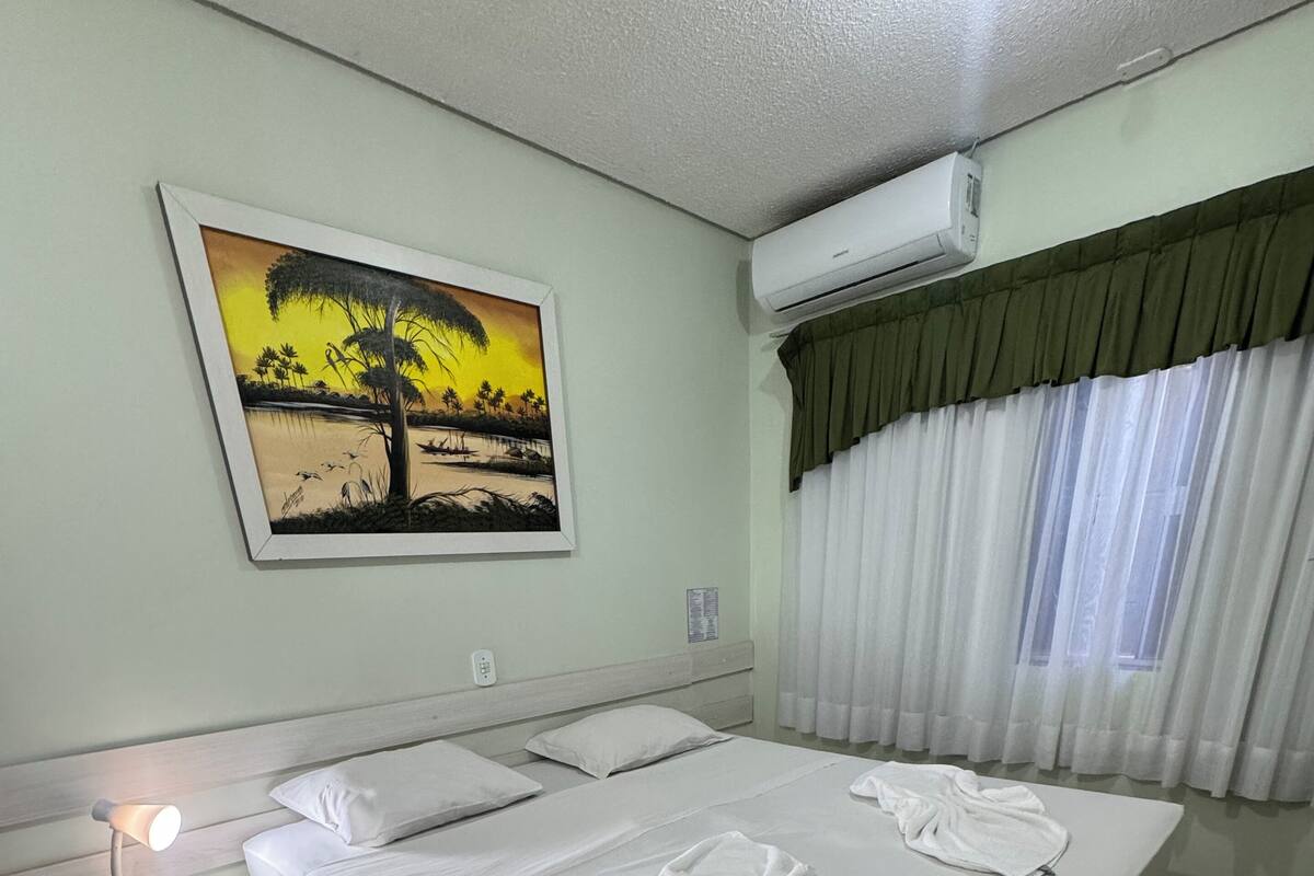 Une chambre d’hôtel bien aménagée, avec un grand lit, une table de chevet avec une lampe, un tableau au mur et un appareil de climatisation.