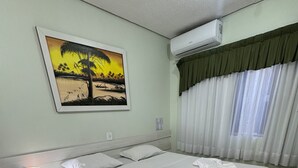 Une chambre d’hôtel bien aménagée, avec un grand lit, une table de chevet avec une lampe, un tableau au mur et un appareil de climatisation.