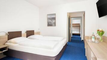Een hotelkamer met twee bedden, een bureau met een fles en glazen, een televisie en een foto aan de muur.