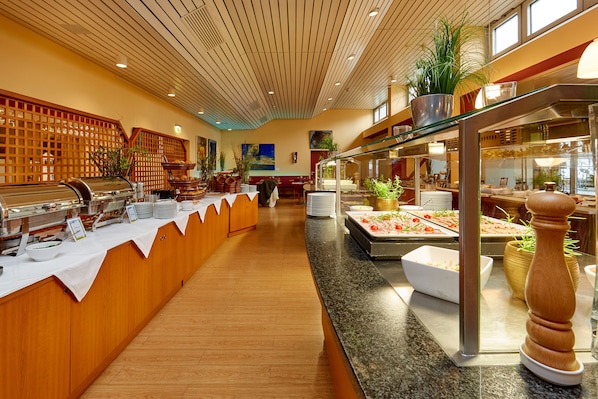 A buffet area with a variety of food stations, wooden paneling, and potted plants. - Hotel Bayern Vital (Bad Reichenhall)