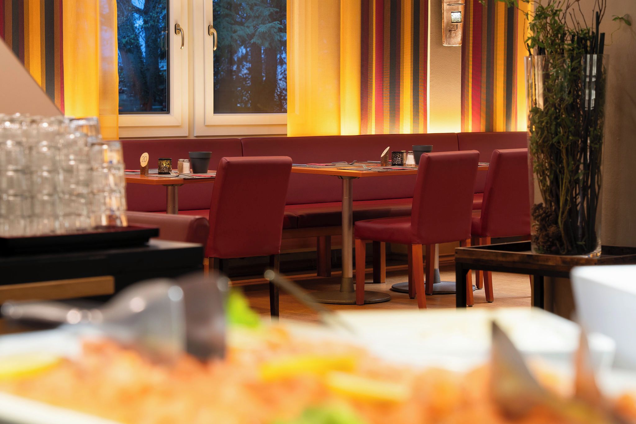 Ein Restaurantinneres mit Sitzecken, Tischen und einem großen Fenster mit Blick auf Bäume.
