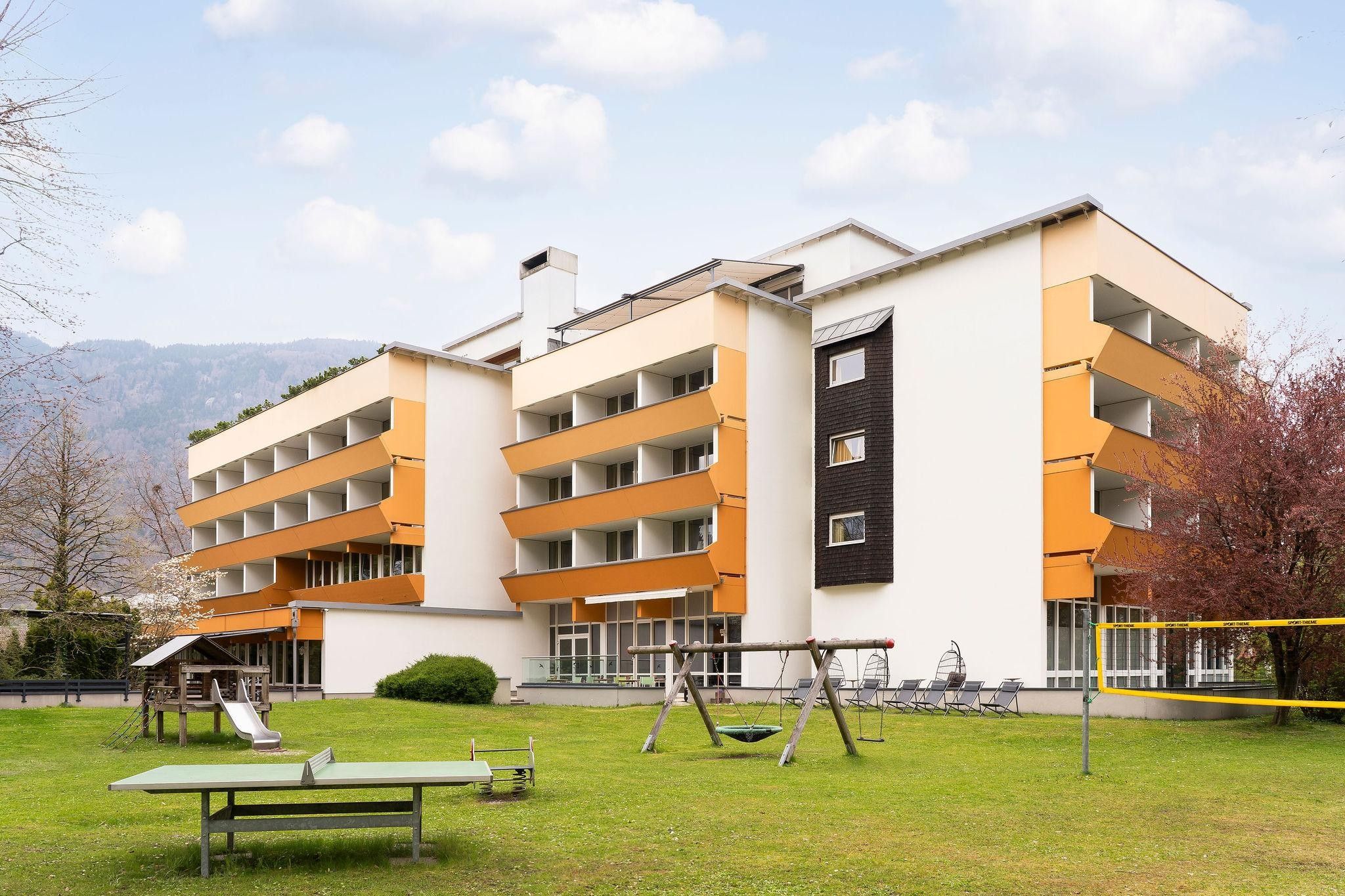 A multi-story building with a flat roof, a playground with swings and a slide, and a tennis court.
