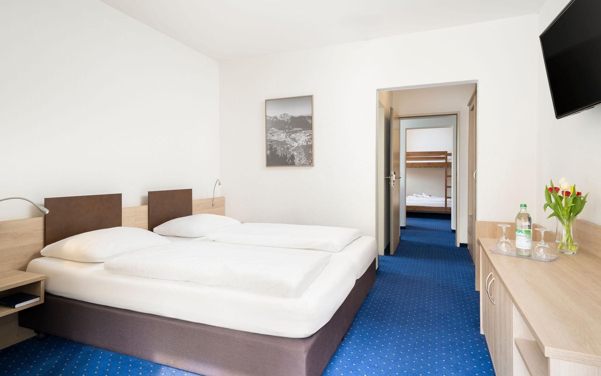 Habitación de hotel con cama doble, escritorio con silla, televisor montado en la pared y un cuadro de un paisaje.